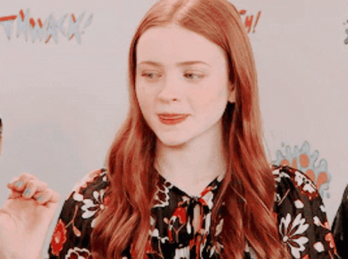 A Woman With Red Hair Is Wearing A Floral Top GIF