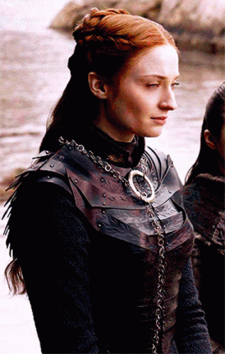 A Woman With Red Hair Is Wearing A Leather Armor And A Necklace With The Letter O On It GIF