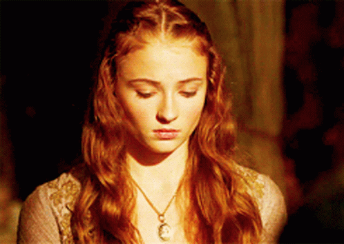 A Woman With Red Hair Is Wearing A Necklace With A Pendant On It GIF