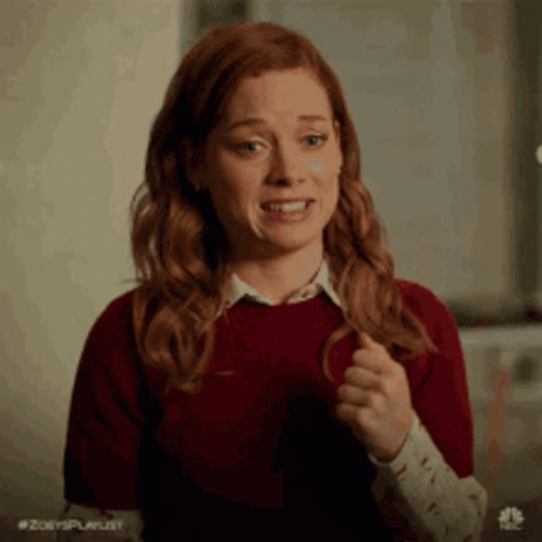 A Woman With Red Hair Is Wearing A Red Sweater And A White Shirt And Is Making A Funny Face . GIF