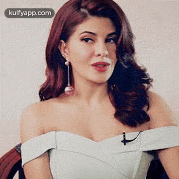 A Woman With Red Hair Is Wearing A White Dress And Earrings . GIF
