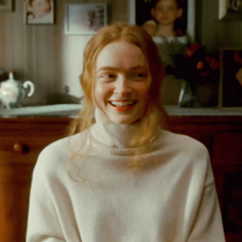 A Woman With Red Hair Is Wearing A White Turtleneck And Smiling GIF