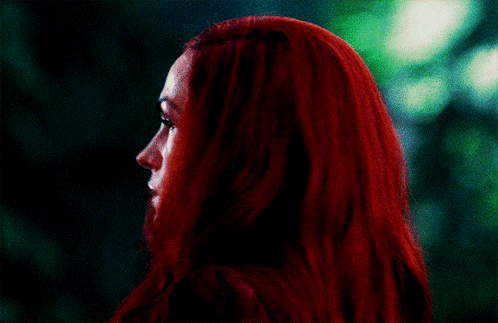 A Woman With Red Hair Looks At The Camera With A Green Background GIF