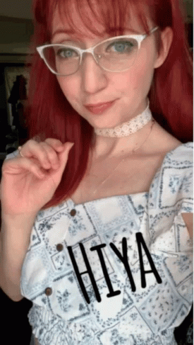 A Woman With Red Hair Wearing Glasses And A Choker Has The Word Hiya Written On Her Top GIF