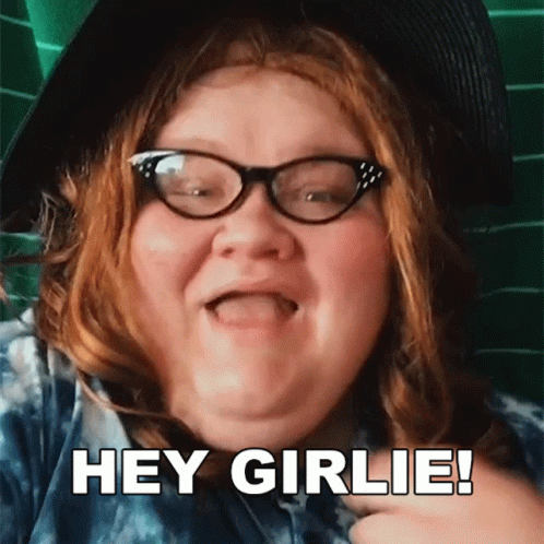 A Woman With Red Hair Wearing Glasses And A Hat Says Hey Girlie GIF