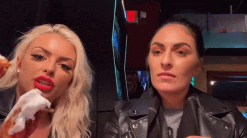 A Woman With Red Lips Is Eating A Donut Next To Another Woman In A Black Leather Jacket GIF