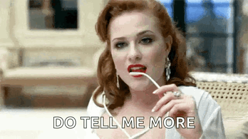 A Woman With Red Lips Is Holding A Pair Of Glasses In Her Mouth And Saying `` Do Tell Me More '' . GIF