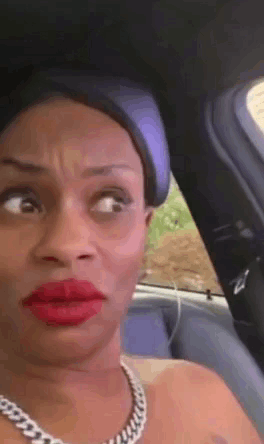 a woman with red lipstick and a necklace is sitting in a car making a funny face
