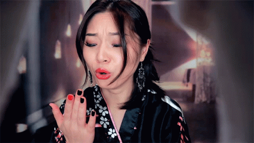 A Woman With Red Lipstick And Black Nail Polish Blows A Kiss GIF