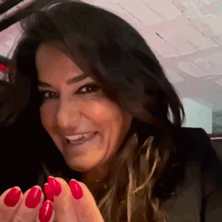 A Woman With Red Nails Is Smiling And Looking At The Camera . GIF