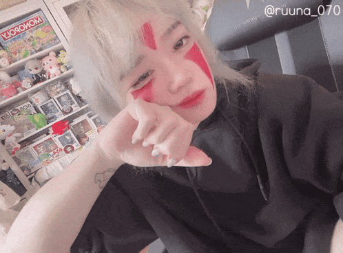 a woman with red paint on her face is standing in front of a shelf with a monopoly game