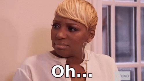 A Woman With Short Blonde Hair Is Sitting In Front Of A Window And Making A Face . GIF