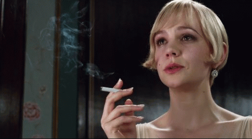 A Woman With Short Blonde Hair Is Smoking A Cigarette In A Dark Room GIF