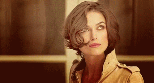 A Woman With Short Brown Hair Is Wearing A Brown Jacket And Looking Up . GIF