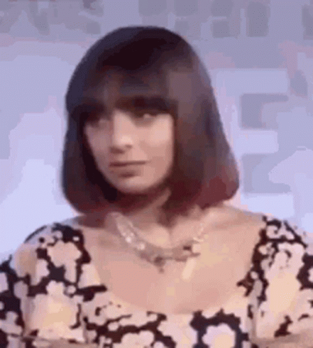 A Woman With Short Hair And A Necklace Is Wearing A Black And White Dress . GIF