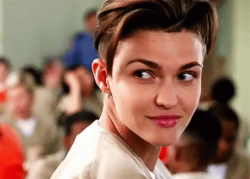 A Woman With Short Hair And A Shaved Head Is Looking At The Camera In Front Of A Crowd Of People . GIF