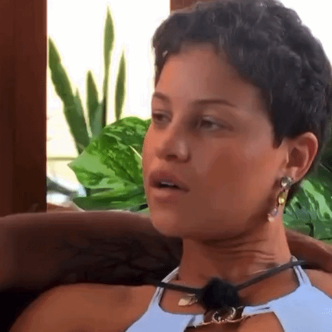 A Woman With Short Hair Is Sitting In A Chair Wearing A Necklace And Earrings . GIF