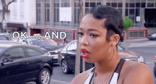A Woman With Short Hair Is Standing On A Street With Cars Parked In Front Of Her . GIF