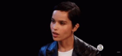 A Woman With Short Hair Is Wearing A Leather Jacket And Earrings And Making A Funny Face . GIF
