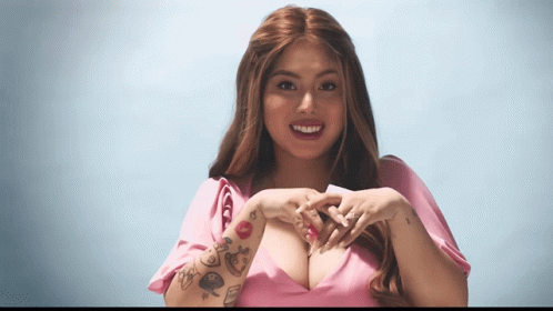 A Woman With Tattoos On Her Arm Making A Heart Shape With Her Hands GIF