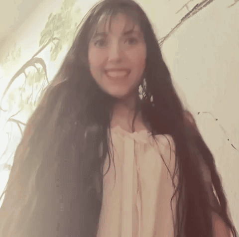 A Woman With Very Long Hair Is Smiling And Looking At The Camera GIF