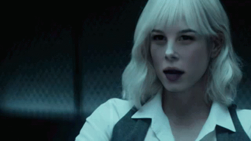 A Woman With White Hair Is Sitting In A Dark Room With Her Tongue Hanging Out . GIF