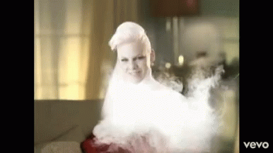 A Woman With White Hair Is Surrounded By Smoke And The Word Vevo Is On The Bottom Right GIF