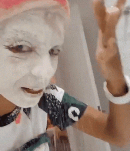 A Woman With White Paint On Her Face Is Taking A Selfie With Her Phone . GIF