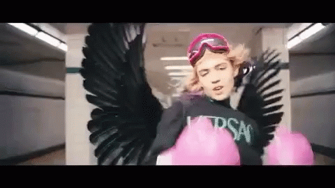 A Woman With Wings And Pink Boxing Gloves Is Wearing A Black Shirt And Goggles . GIF