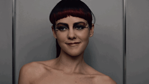 A Woman Without A Shirt Is Wearing Black Eye Shadow And Red Hair GIF