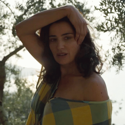 A Woman Wrapped In A Plaid Shirt Is Standing In Front Of A Tree GIF