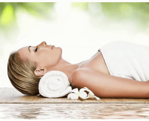 A Woman Wrapped In A Towel Is Laying On A Wooden Table GIF