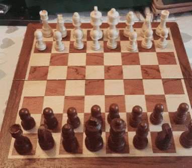 A Wooden Chess Board With White And Brown Chess Pieces On It GIF
