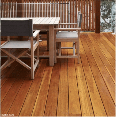 A Wooden Deck With A Table And Chairs And A Fence Behind It GIF