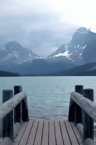 A Wooden Dock With Mountains In The Background And A Lake In The Foreground GIF