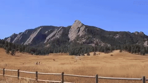 A Wooden Fence Surrounds A Grassy Field With Mountains In The Background GIF
