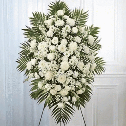 A Wreath Of White Flowers And Green Leaves Is Sitting On A Stand In Front Of A Door . GIF