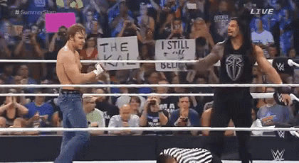 A Wrestler Holding A Sign That Says The Kill Is Standing In A Wrestling Ring With Another Wrestler . GIF