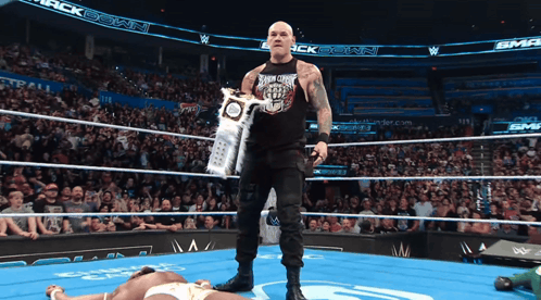 A Wrestler Holds A Trophy In A Wrestling Ring With A Crowd Watching GIF
