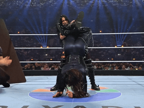 A Wrestler Holds Another Wrestler Upside Down On Her Back GIF