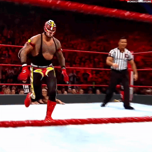 A Wrestler In A Mask And Boxing Gloves Is Running In A Ring With A Referee GIF