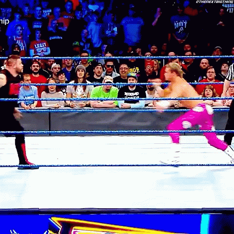 A Wrestler In A Pink Outfit Is Jumping Into The Ring While A Crowd Watches GIF