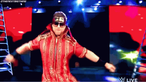 A Wrestler In A Red Outfit And Sunglasses Is Dancing On A Stage . GIF
