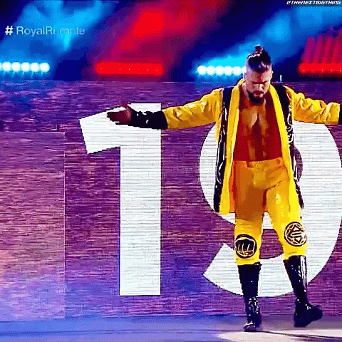 A Wrestler In A Yellow Jacket And Pants Is Standing In Front Of A Sign That Says 19 . GIF