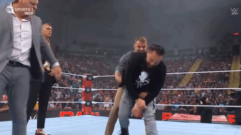 A Wrestler Is Being Helped Out Of The Ring By A Man In A Suit GIF