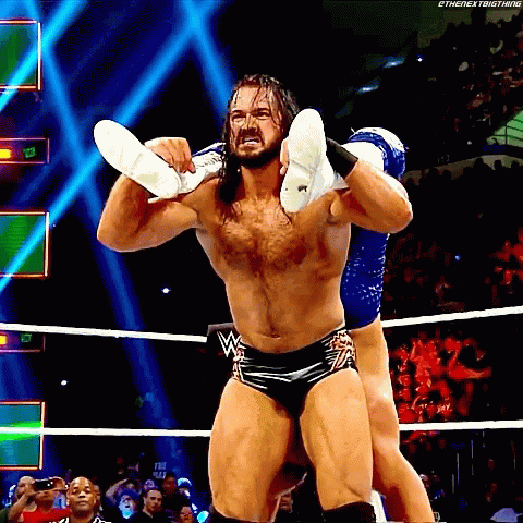 A Wrestler Is Carrying Another Wrestler On His Shoulders During A Match GIF