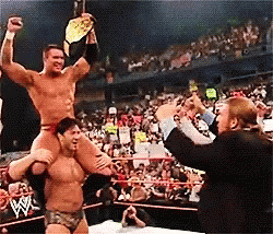 A Wrestler Is Carrying Another Wrestler On His Shoulders In A Ring GIF