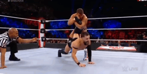 A Wrestler Is Doing Push Ups In A Wrestling Ring While A Referee Looks On . GIF