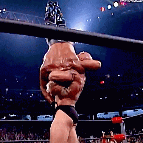 A Wrestler Is Hanging Upside Down In The Air While Another Wrestler Holds Him . GIF