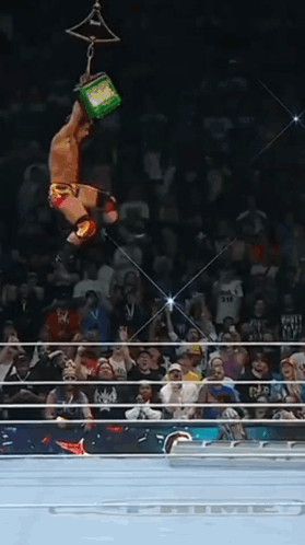 A Wrestler Is Hanging Upside Down In The Air While Holding A Green Box GIF